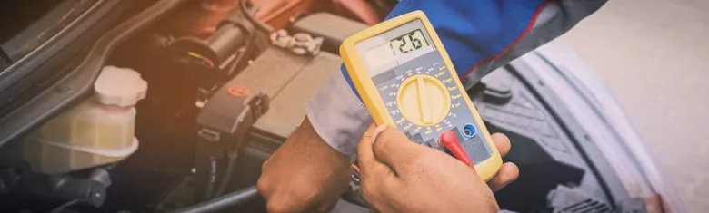 Mechanik měří napětí autobaterie multimetrem pod kapotou auta.