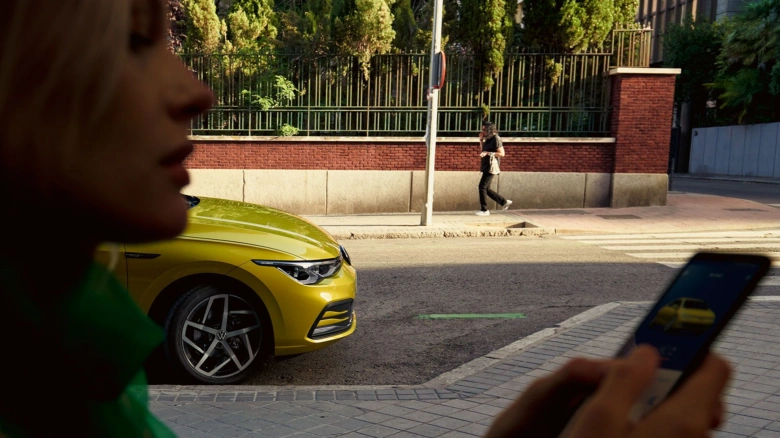 Žena s žlutým VW autem používá telefon na ulici.