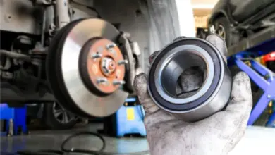 Mechanik drží ložisko kola při opravě pod autem.