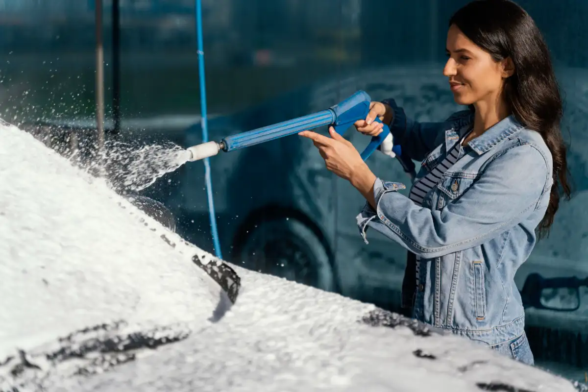 Žena umývá auto v samoobslužné myčce pomocí pěnové pistole.