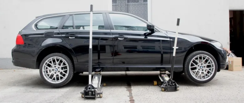 Černé auto zvedané dvěma zvedáky pod rámem na ploché povrchu.