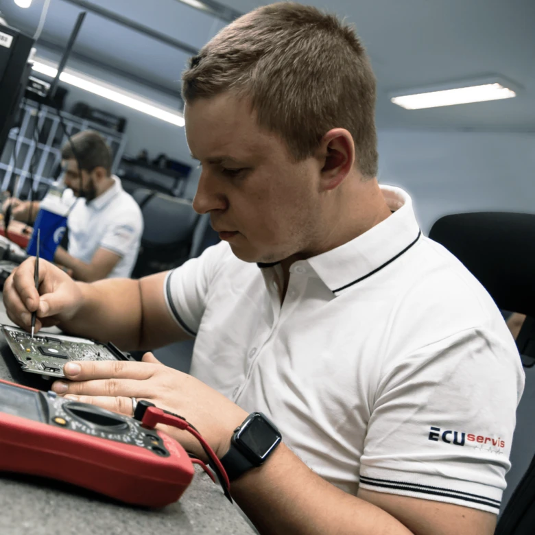 Mechanik opravuje řídící jednotku motoru v dílně s multimetrem.