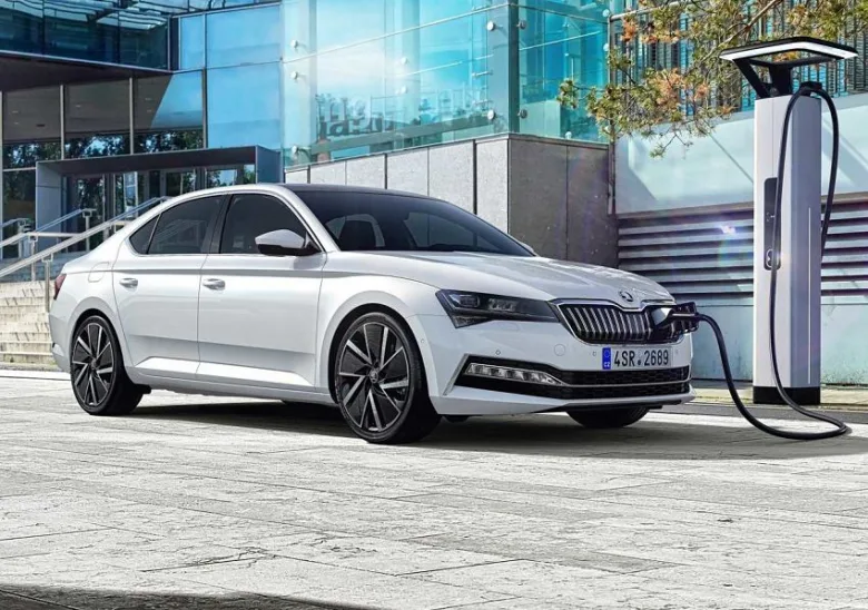 Bílý elektromobil Škoda nabíjen na veřejné stanici v městském prostředí.