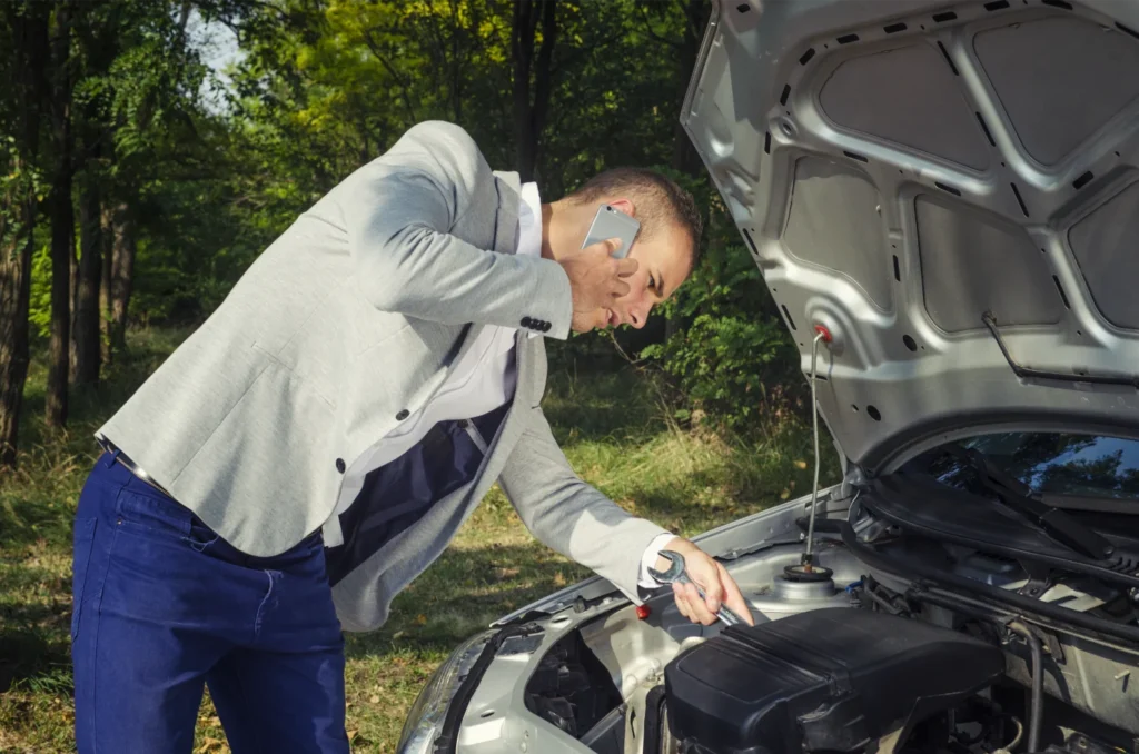 Muž opravuje motor auta venku a řeší problém s benzínem.