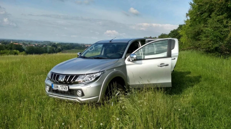 Stříbrný Mitsubishi L200 s otevřenou dveřmi na trávníku.