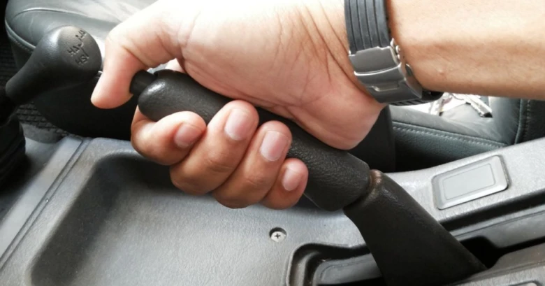 Ruka drží páku ruční brzdy v automobilu s automatikou.