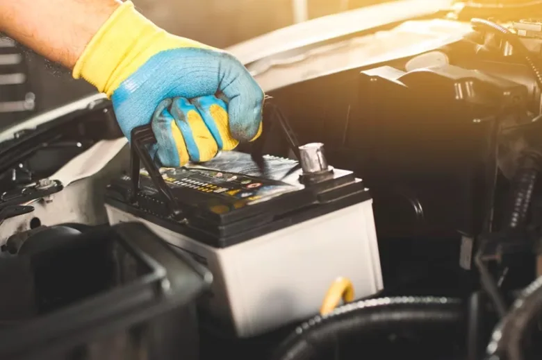 Ruční instalace nové automobilové baterie do motorového prostoru.