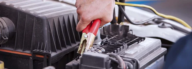 Ruční připojení červeného klemového kabelu na automobilový akumulátor.