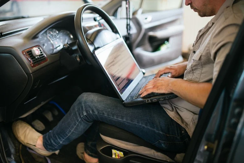 Muž v autě používá notebook pro diagnostiku chybových kódů.