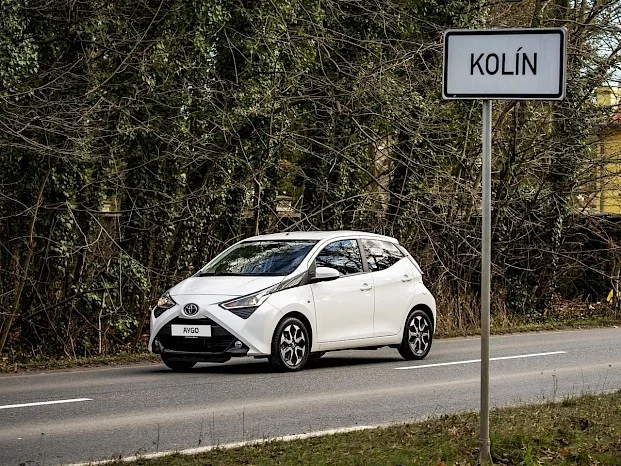 Bílý automobil Toyota jezdí po silnici u lesa.