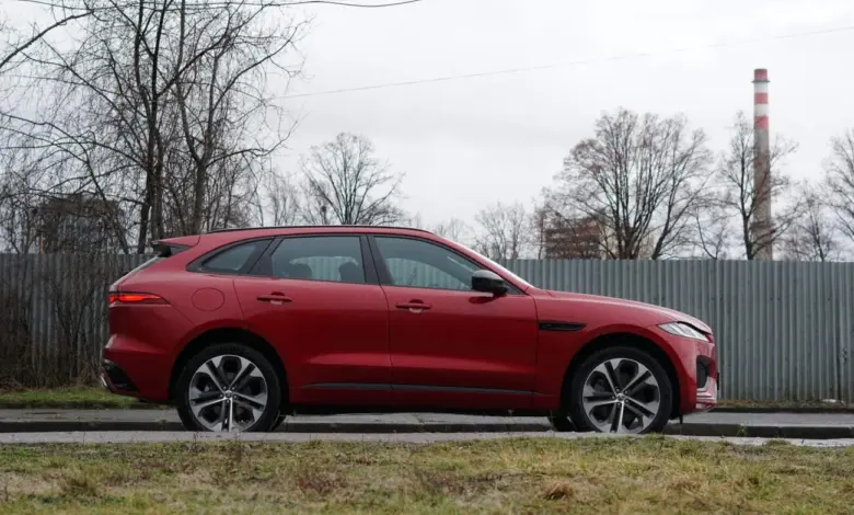 Červený SUV Jaguar F-Pace z boku na silnici.