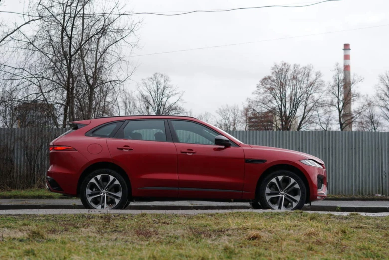 Červený SUV Jaguar F-Pace z boku na silnici.