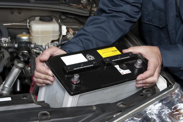 Mechanik montuje autobaterii do motorového prostoru vozu.