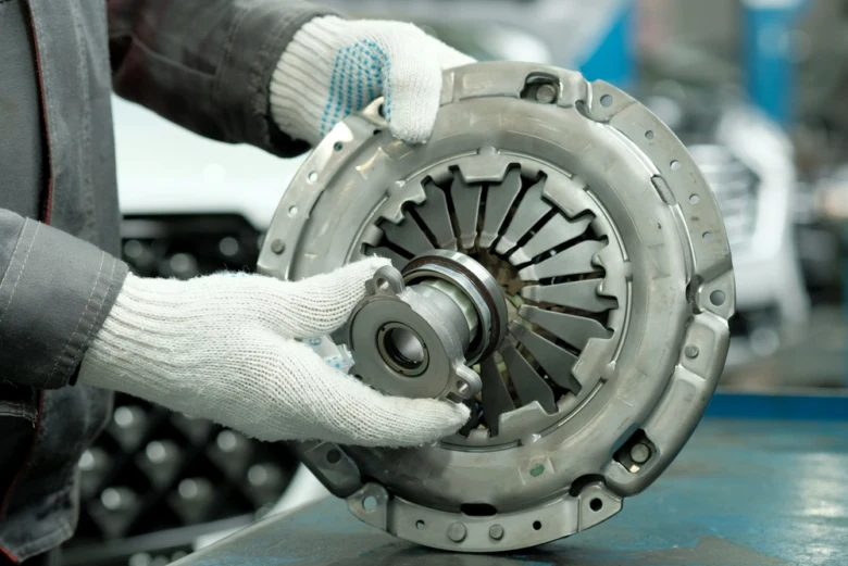 Mechanik drží spojku automobilu v rukavicích pro kontrolu.