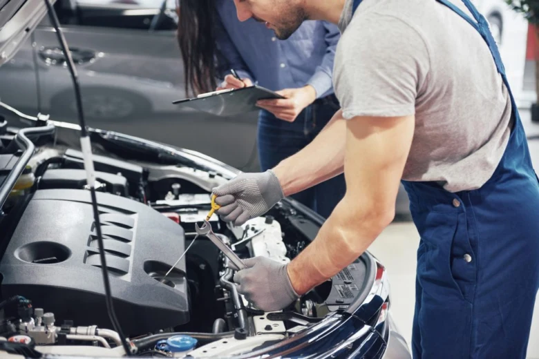 Mechanik opravuje auto s otevřenou kapotou pomocí klíče.