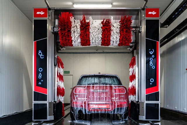 Červené auto v automatizované myčce s velkými štětcemi.