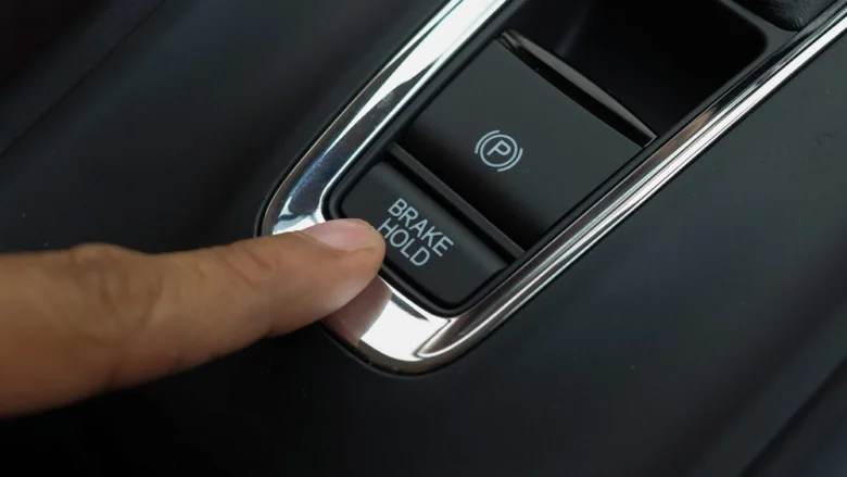 Prst tlačí na držák brzdy vedle elektronického parkovacího brzdového systému.