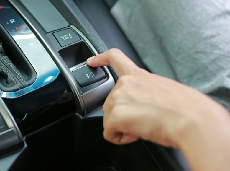 Ruka tlačí na elektronický parkovací brzdu v interiéru auta s automatickou převodovkou.