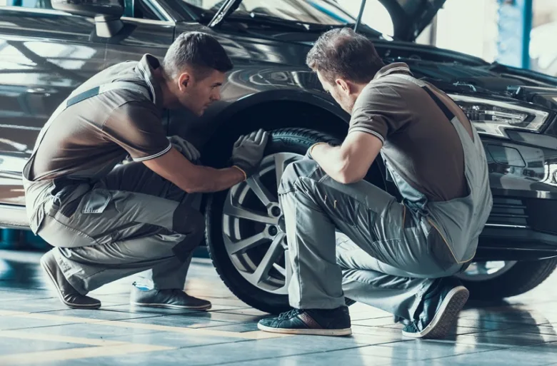 Mechanici opravují kolo černého auta v dílně.