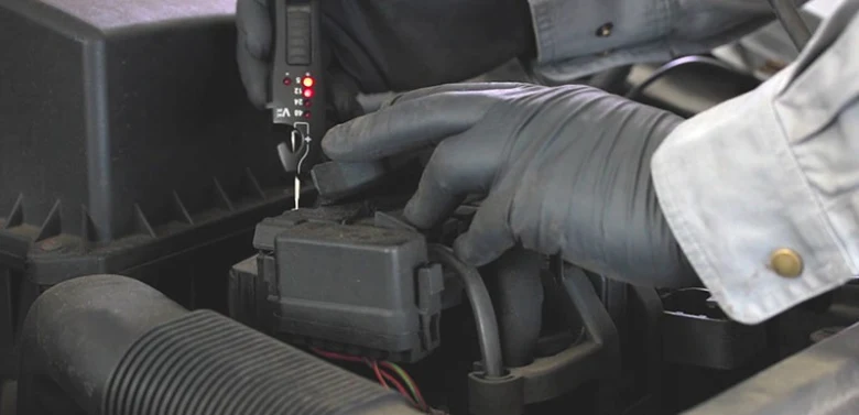 Technik testuje zapalovací cívku multimetrem pod kapotou.