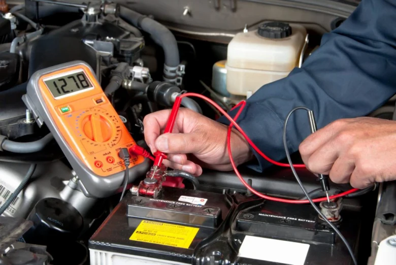Mechanik měří napětí autobaterie multimetrem pod kapotou.