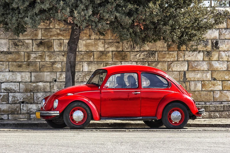Červený klasický VW Bug zaparkovaný u kamenné zdi.