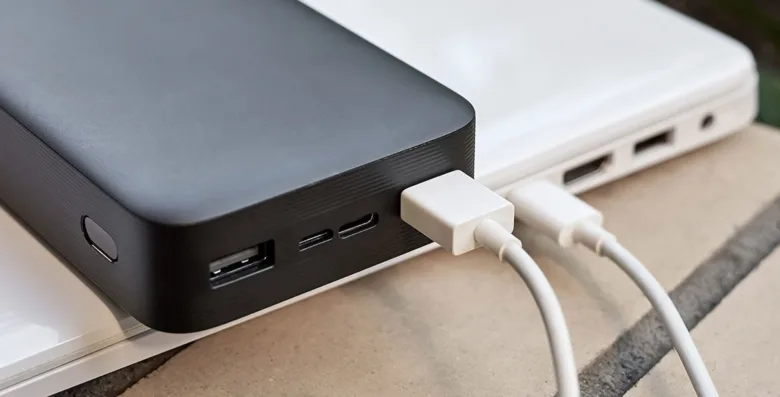 Černý externí baterie nabíjí bílý notebook přes kabely.