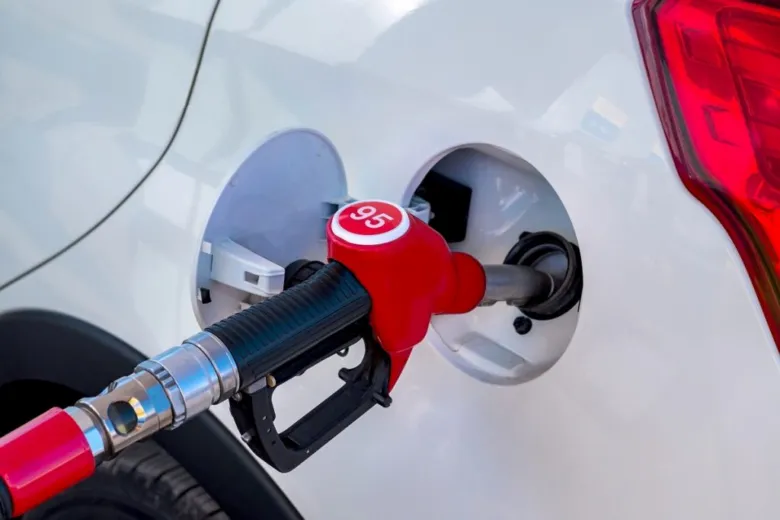 Červená benzínová hadice s označením 95 v nádrži bílého auta.