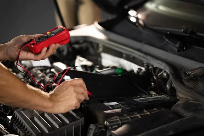 Mechanik měří napětí automobilové baterie multimetrem pod kapotou.