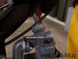 Blízký záběr na karburátor s šroubem pro nastavení hladiny paliva.