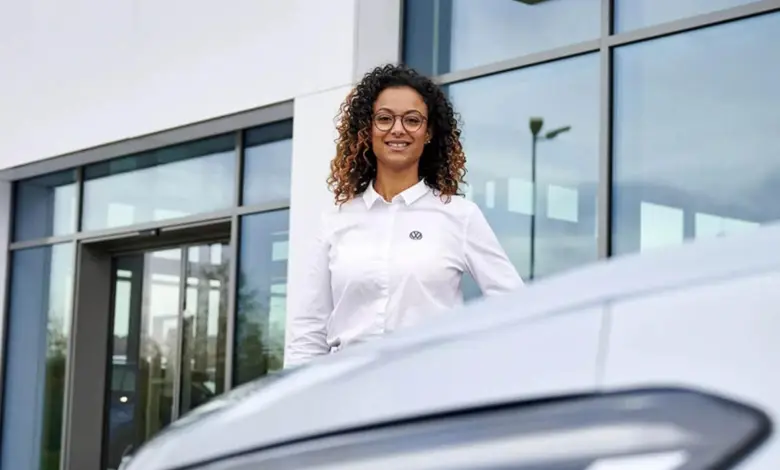 Žena stojí vedle Volkswagenu Golfa před budovou.
