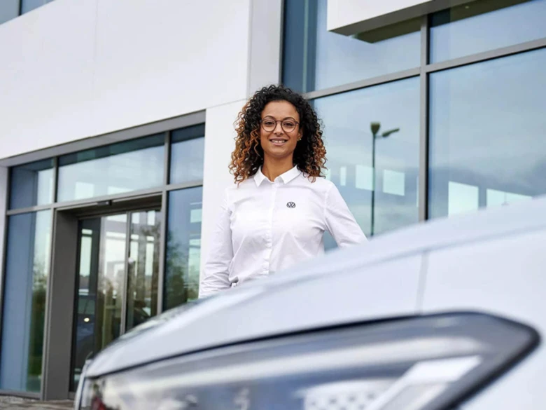Žena stojí vedle Volkswagenu Golfa před budovou.