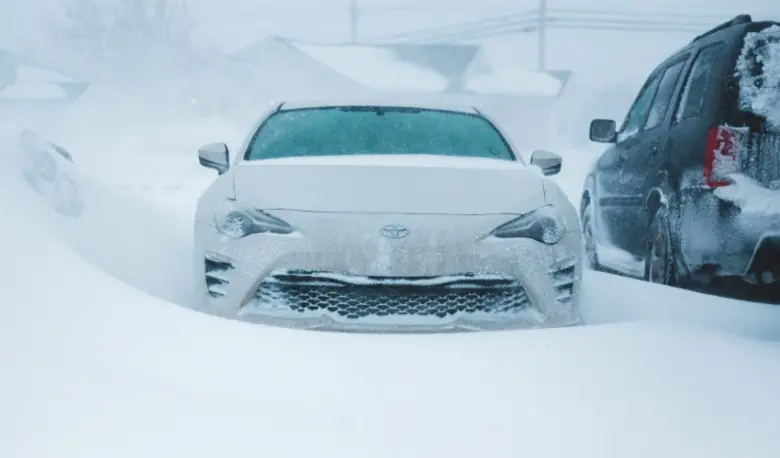 Bílé auto pokryté sněhem v zimní bouři na parkovišti.