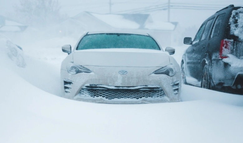 Bílý auto zakryté sněhem na zasněžené ulici.