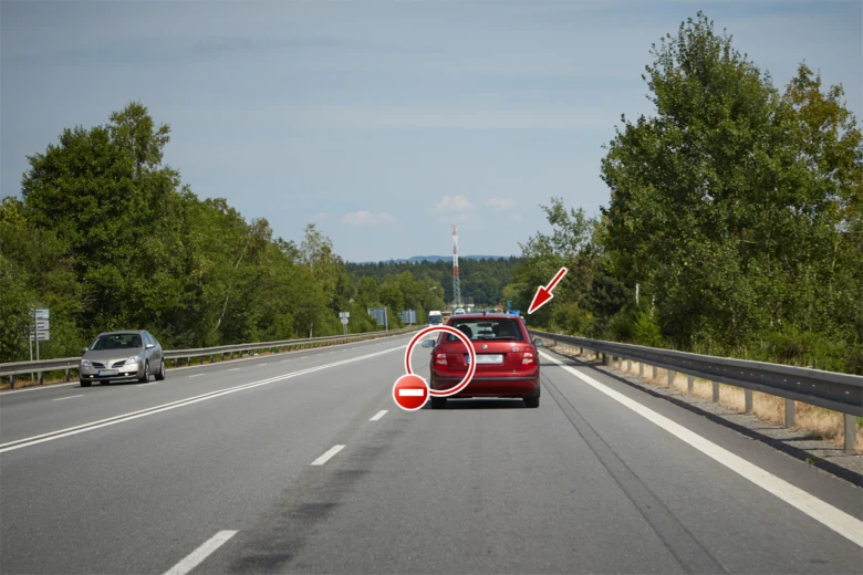 Červené auto zastaveno na dálnici s policistou, ukazuje bezpečnostní situaci.
