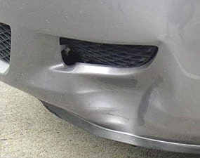 Poškozený stříbrný nárazník automobilu s dřením.