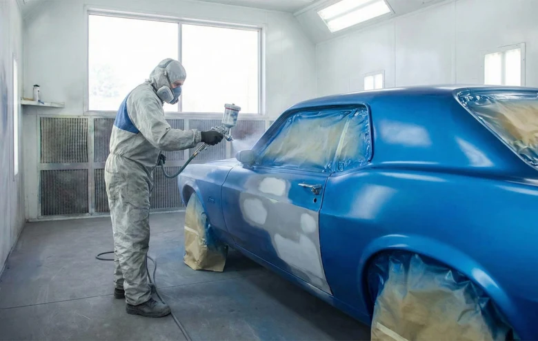 Technik maluje modré auto v barvné komoře s ochranným oblečením.