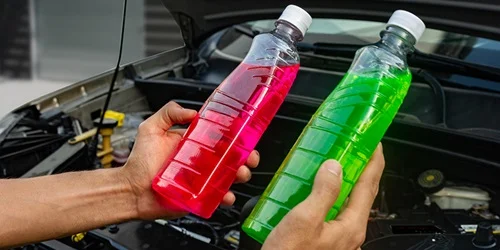 Ruce drží lahve s chladicí tekutinou nad otevřeným motorem auta.