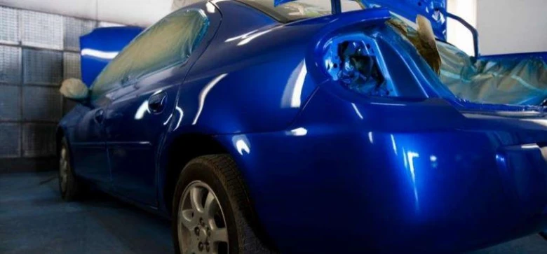 Modrý automobil během profesionálního lakování v dílně.