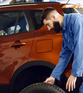 Mechanik opravuje kolo oranžového vozu v dílně.