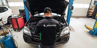 Mechanik kontroluje motor pod otevřenou kapotou vozu v dílně.