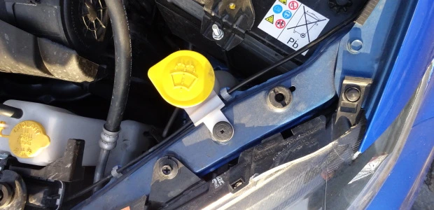 Žlutý víčko nádrže ostřikovače v motorovém prostoru modrého auta.