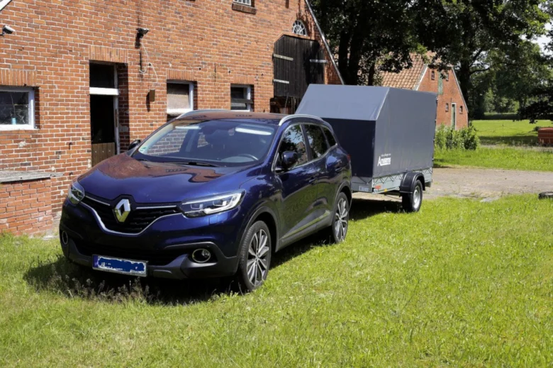 Modrý osobní automobil s přívěsem na trávníku u domu.