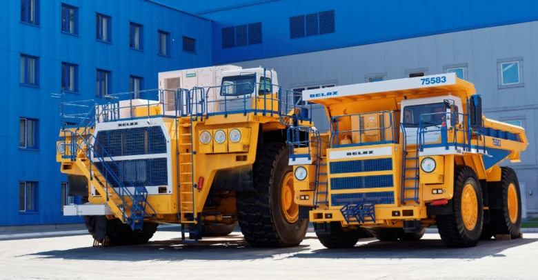 Dva velké žluté těžké nákladní automobily pro dobývání u modré budovy.