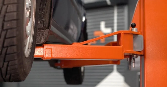 Oranžový zvedák drží auto v servisu pro údržbu převodovky.