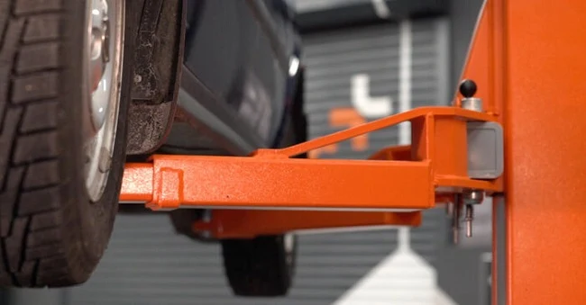Oranžový zvedák drží auto v dílně pro servis převodovky