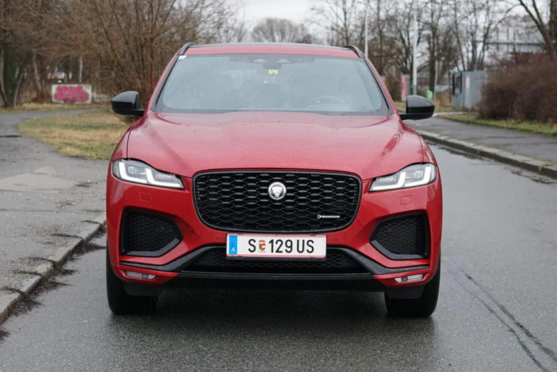 Červený Jaguar F-Pace zepředu na mokré silnici.
