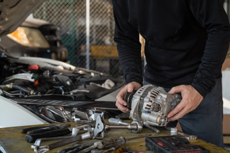 Mechanik drží alternátor při opravě vozu v dílně