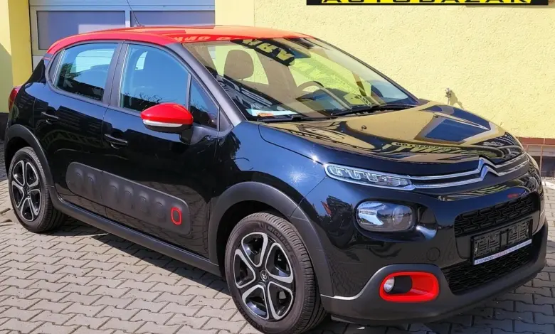 Černý automobil Citroën C3 zaparkovaný na dlažbě před žlutou budovou.