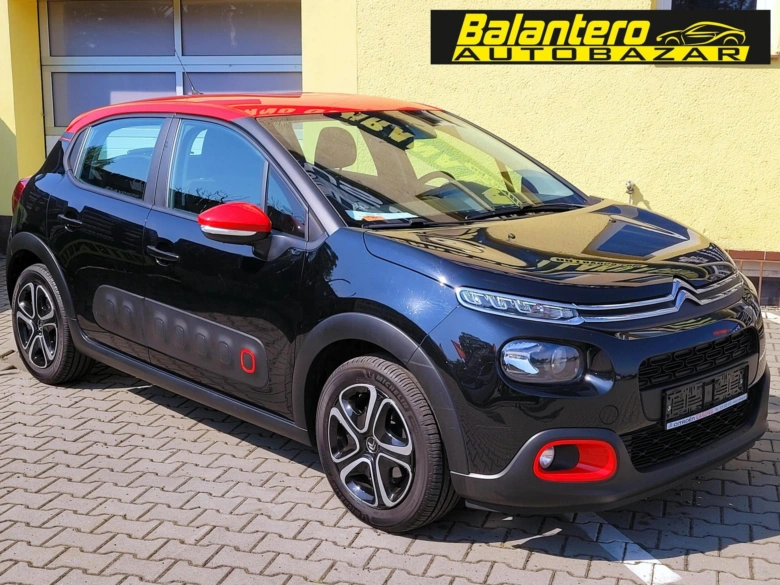 Černý automobil Citroën C3 zaparkovaný na dlažbě před žlutou budovou.